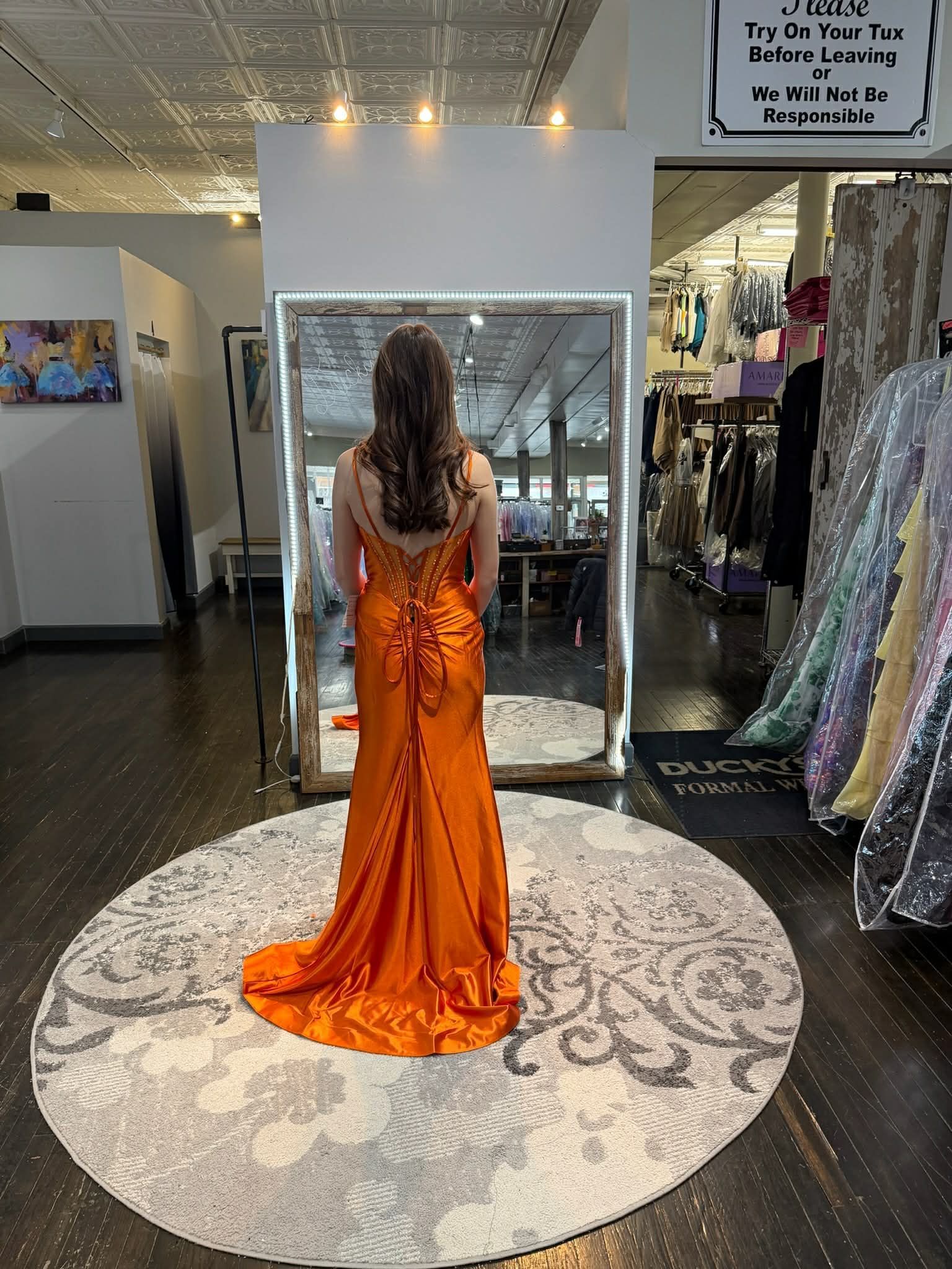 A person stands in a clothing store mirror wearing a floor-length, royal blue gown with intricate silver embroidery.