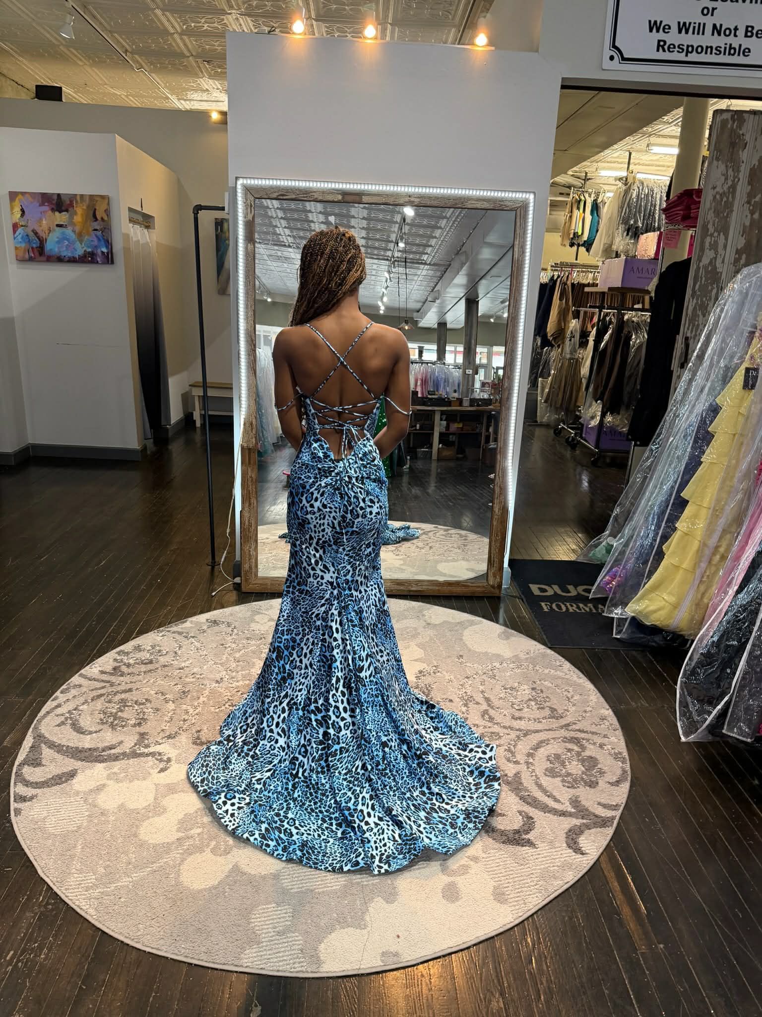 Seven people stand in a clothing store wearing floor-length formal gowns in various colors and styles, smiling together.