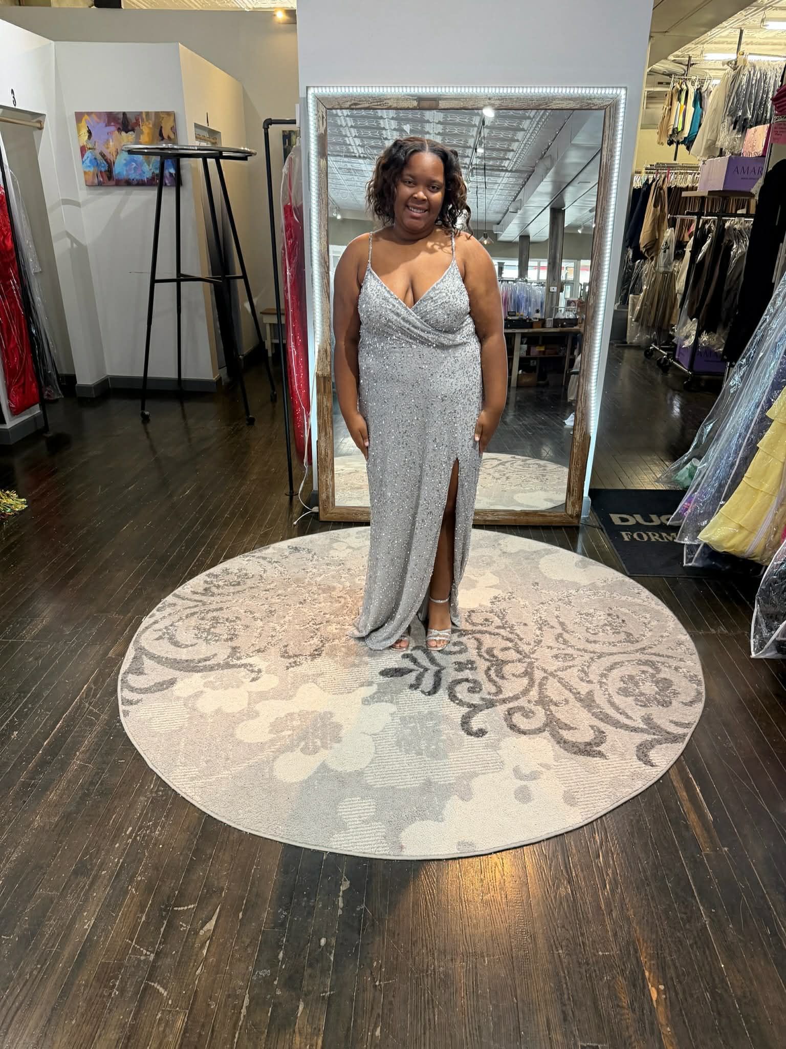 A person stands in a dress shop wearing a floor-length, tiered orange tulle gown with a corset-style bodice.