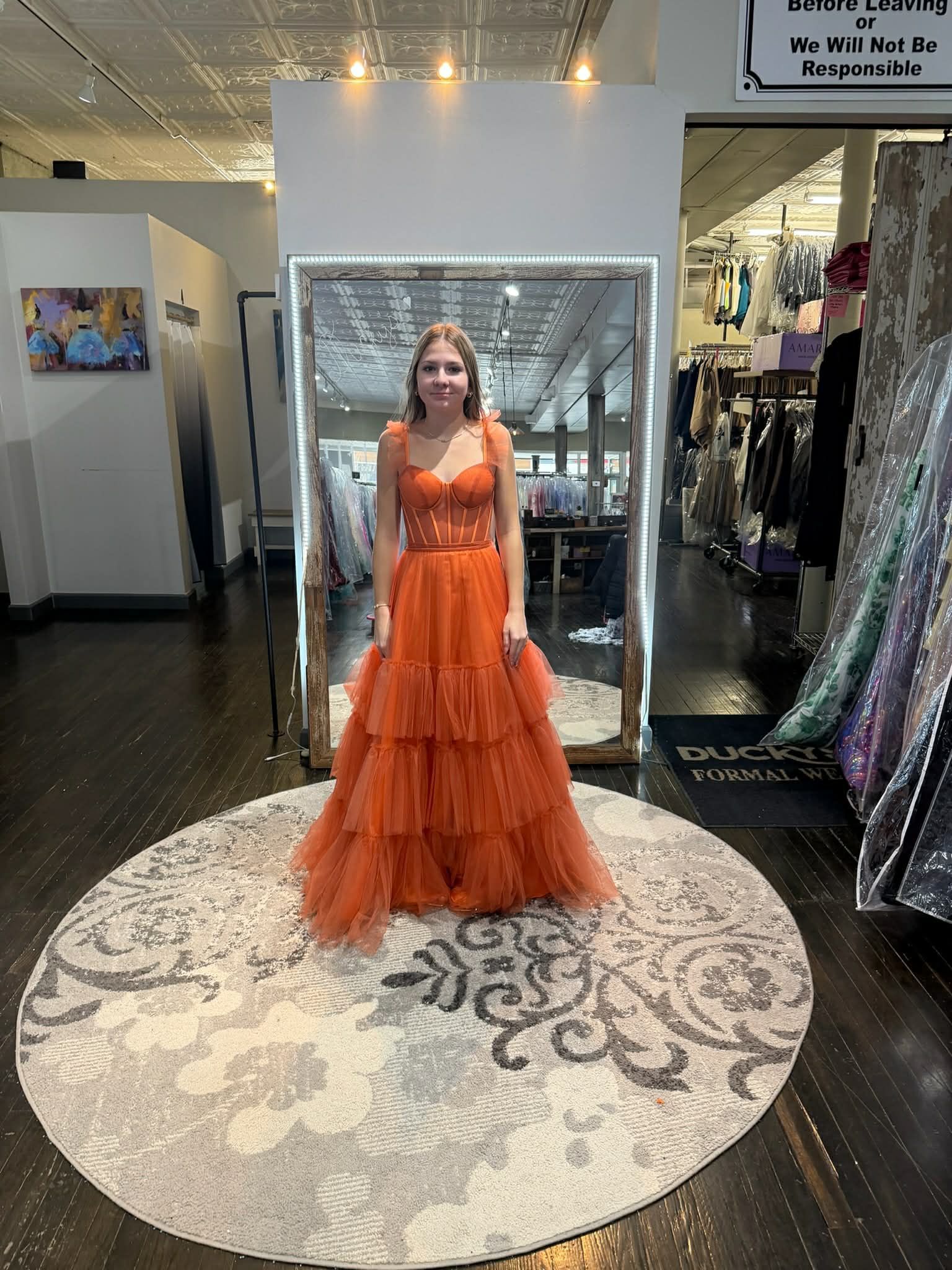 A person in a bridal shop wearing a green and white floral-print gown with a sheer, boned bodice, standing on a rug.