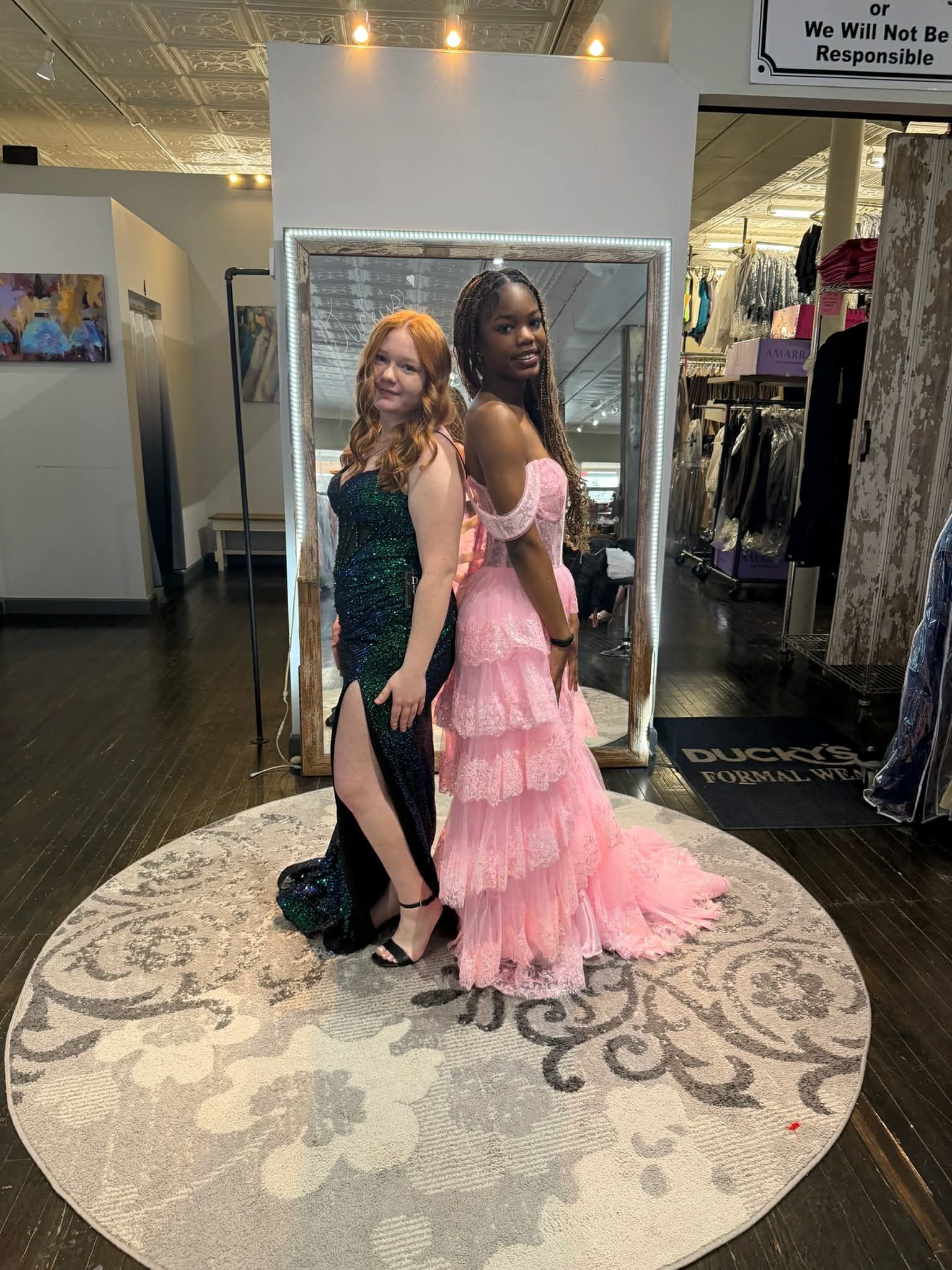 A person stands in a dress shop wearing a floor-length, light blue satin gown with a high slit and jeweled bodice.