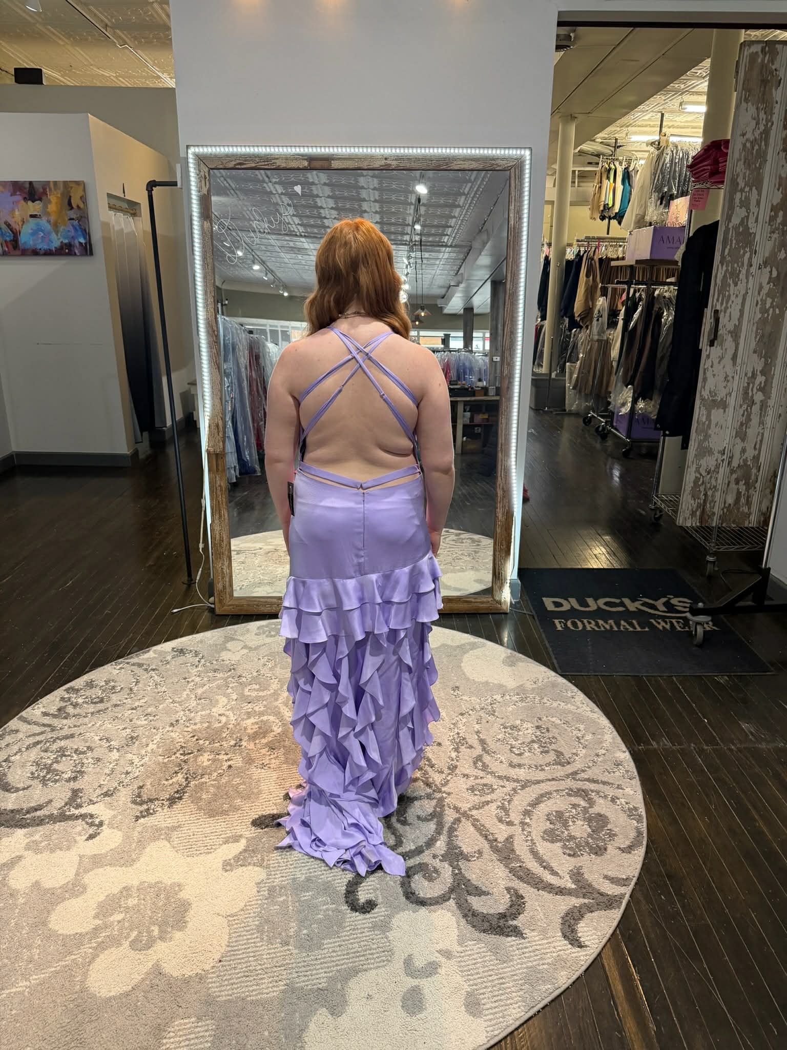 A person in a black, strapless, lace-up mermaid-style evening gown stands in front of a mirror in a clothing boutique.