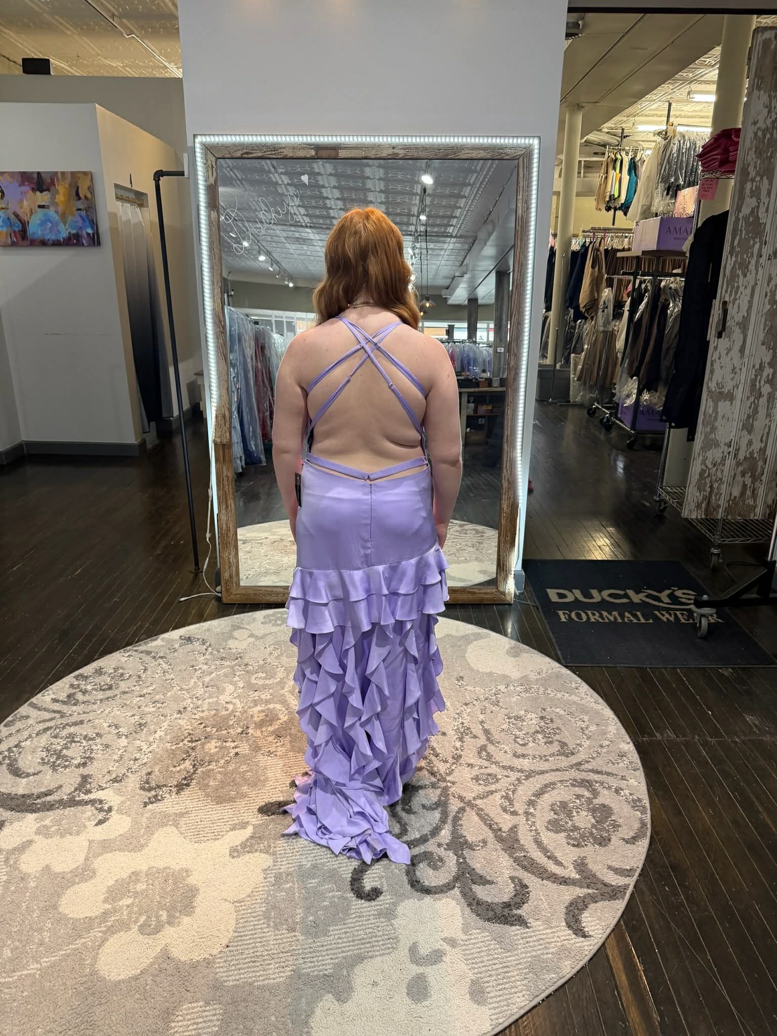 A person stands in a dress shop wearing a floor-length, off-the-shoulder green sequined mermaid gown, seen from behind.