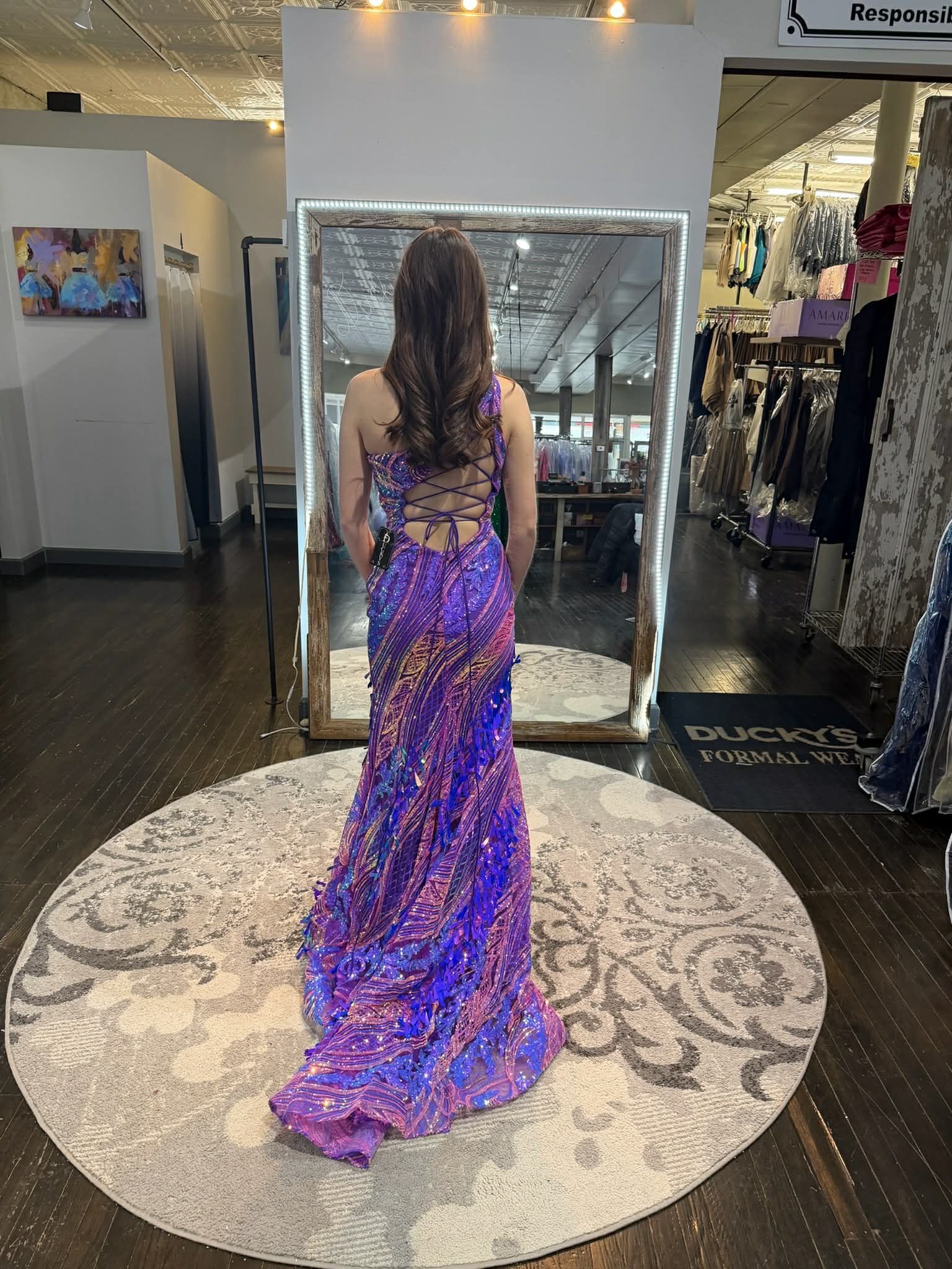 A person wearing a long, maroon, sequined dress standing in front of a mirror in a clothing store.