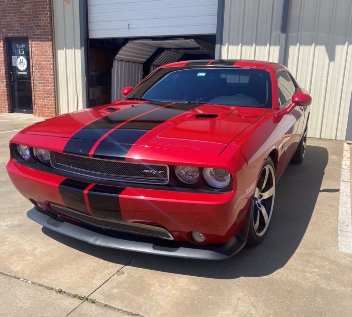 Red Dodge Challenger with black racing stripes parked in front of a garage.
