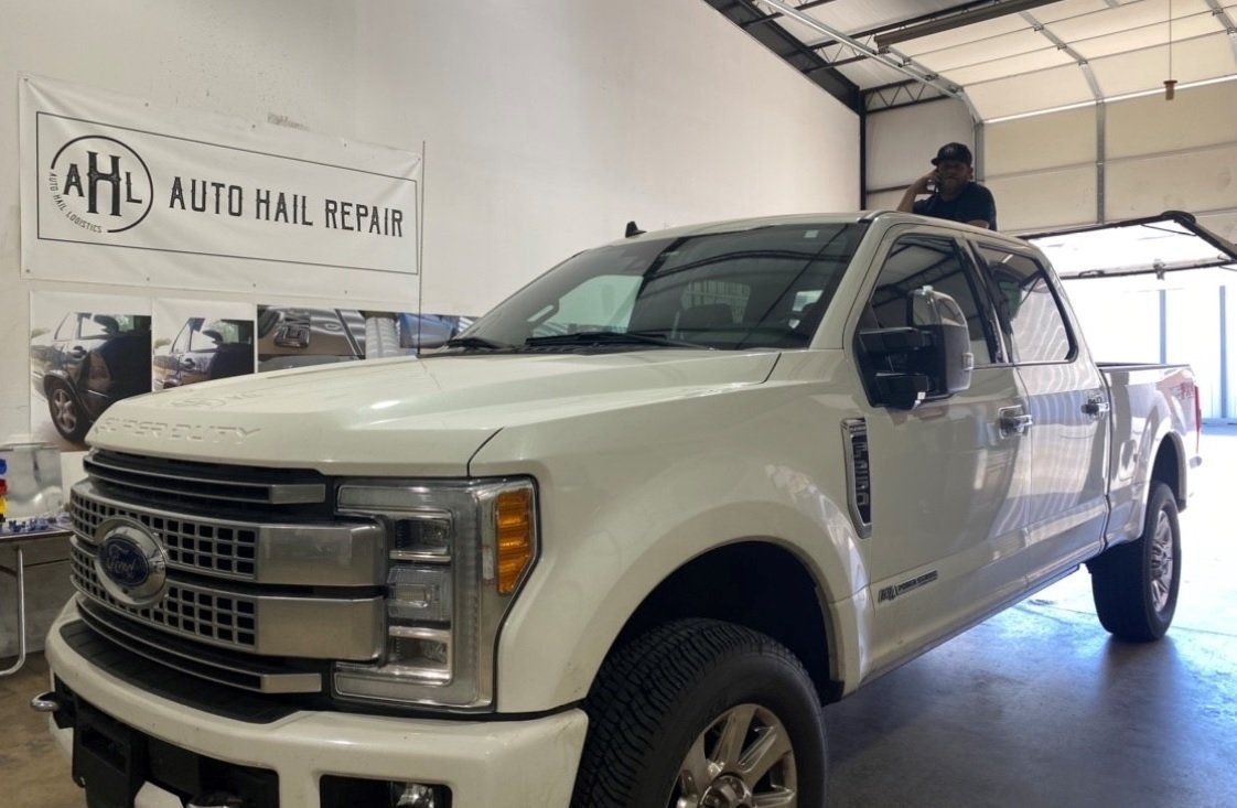 White Ford truck inside a garage with a person on top, banner reads 
