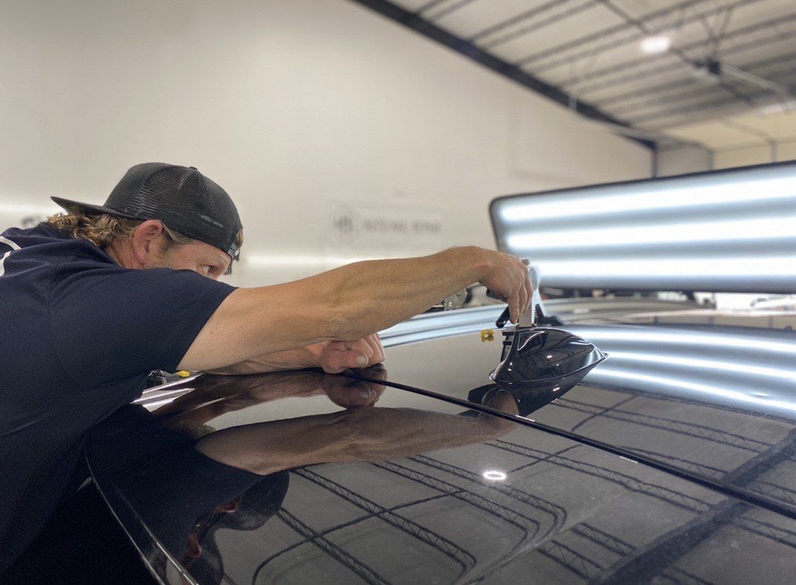 Man using tool to remove dent from car roof in a shop.