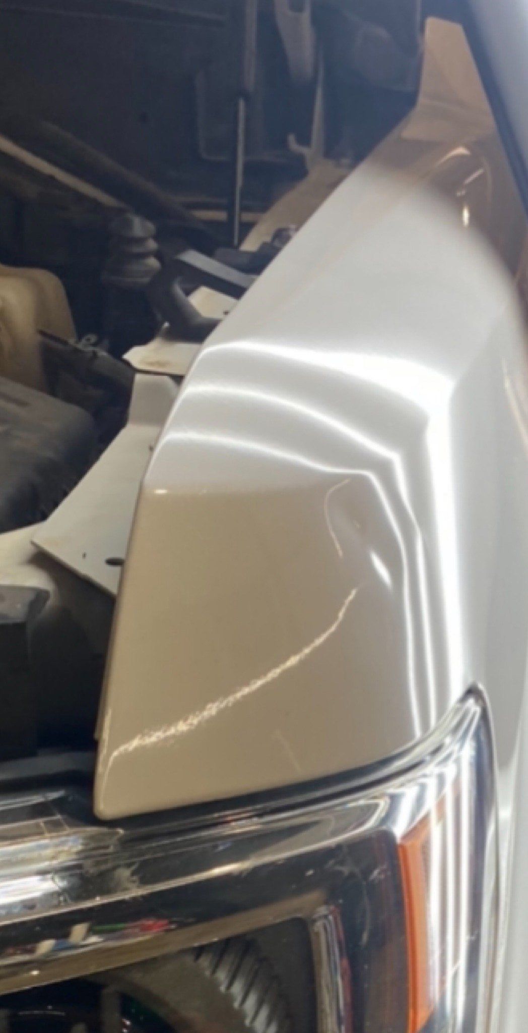 White car fender with a dent, chrome trim, and headlight visible under the open hood.