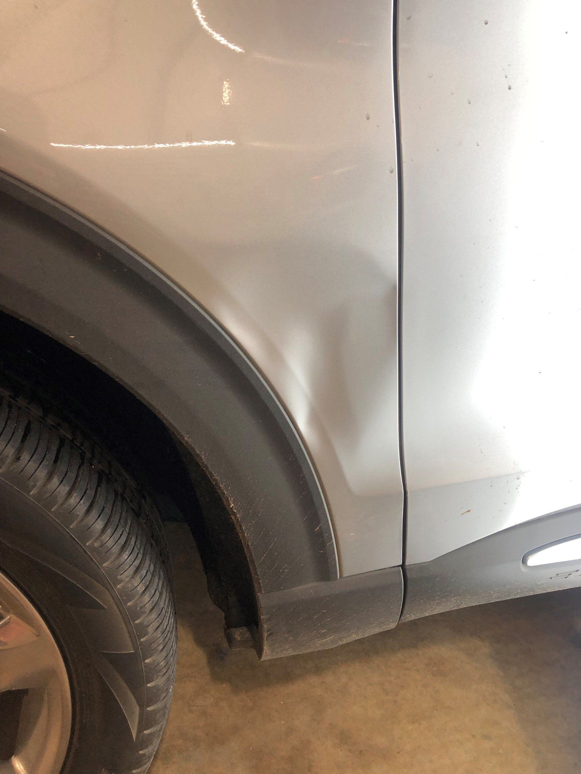 Silver car with dent on front panel. Black wheel arch and tire visible.