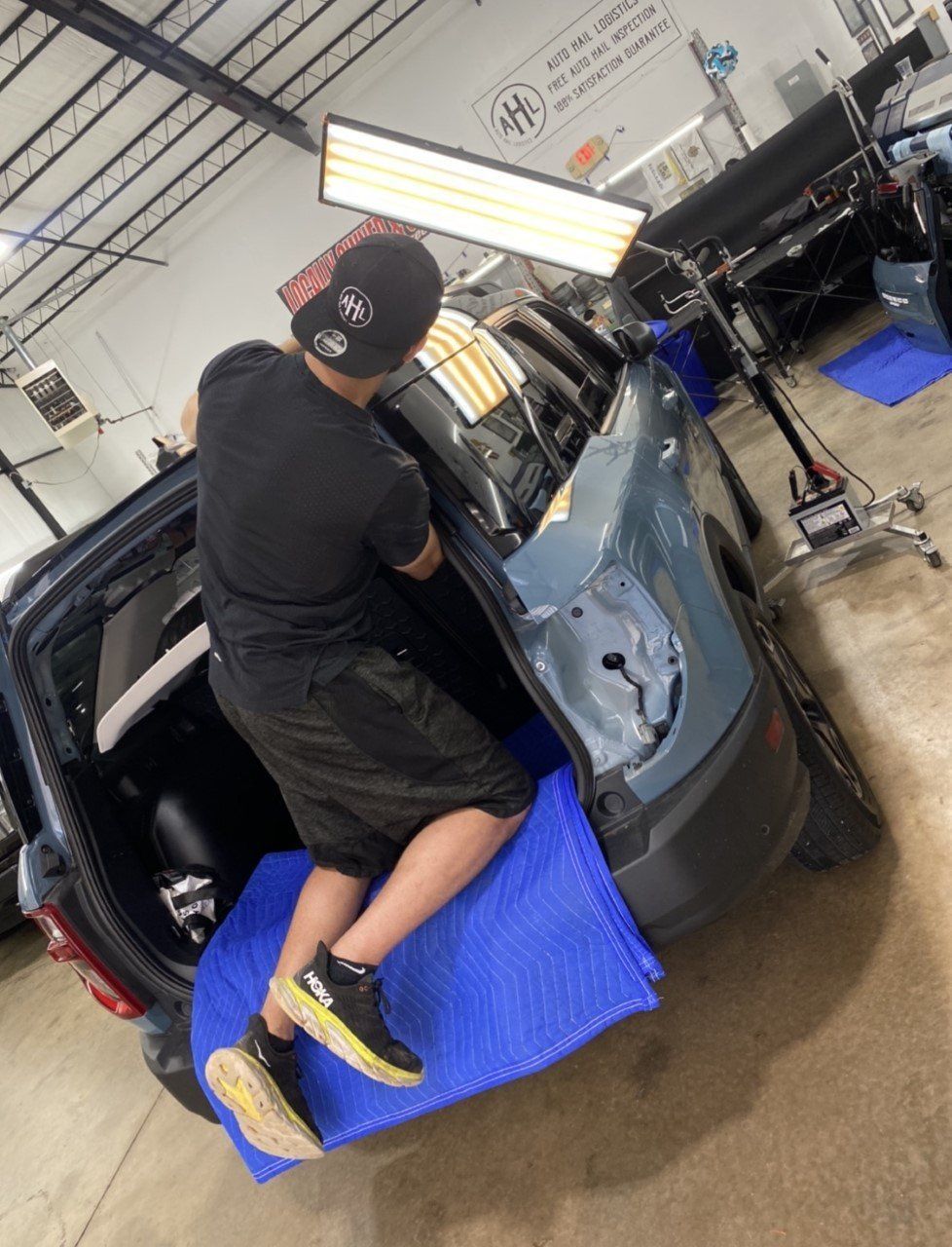 Person repairing a dent in a blue car door inside a repair shop.