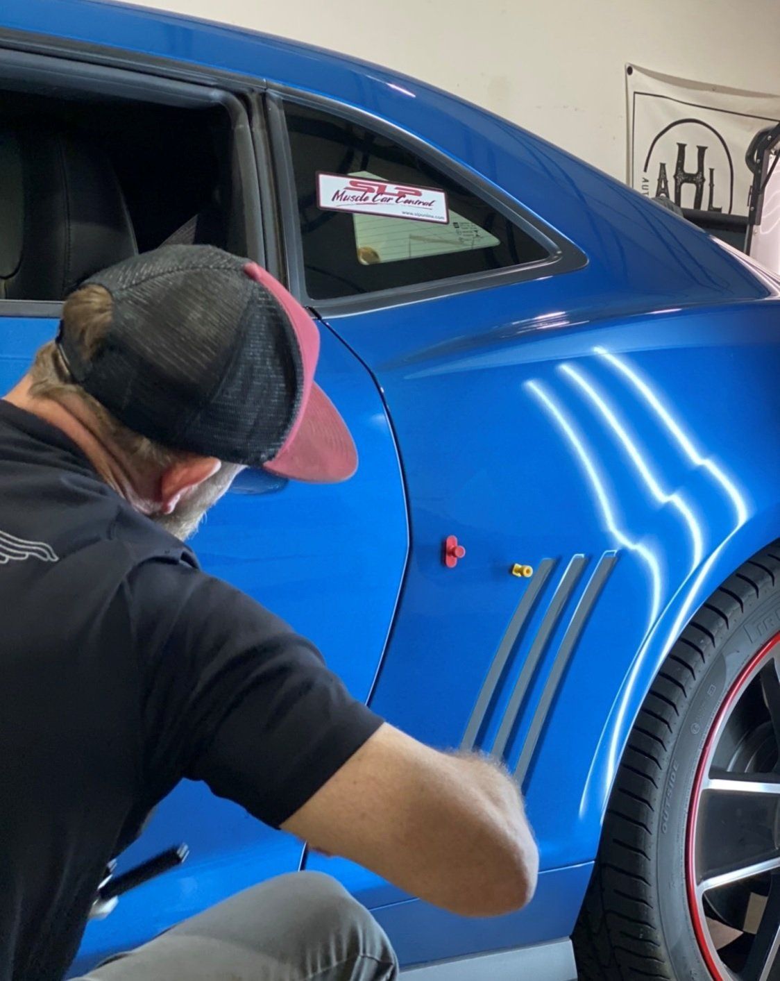 Man working on the blue side panel of a car, with red and grey accents.