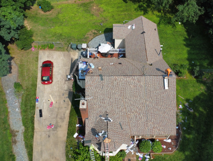 Aerial view of a residential roof replacement in progress with workers, tools, and a red car parked on the driveway.