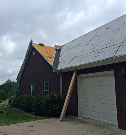 A partially reroofed brick house with new plywood on one section, exposed underlayment on another, and a support beam.