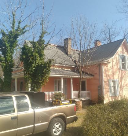 A peach-colored, two-story house with a wraparound porch and a pickup truck parked in the foreground.