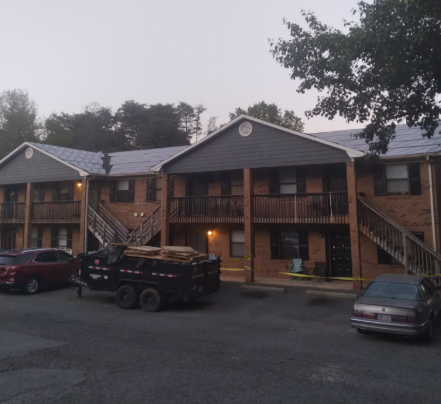 An apartment building undergoing a roof replacement with a dump trailer parked in the parking lot.