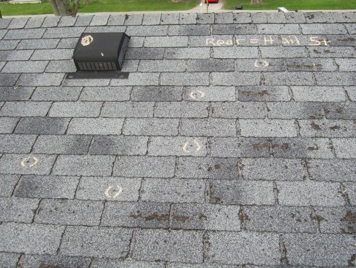 Gray asphalt roof shingles featuring a black attic vent and several white chalk circles highlighting specific spots.