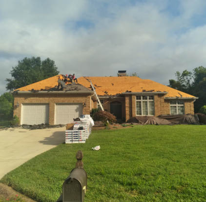 A crew works on a roof renovation, stripping old shingles to reveal the yellow underlayment on a brick house.