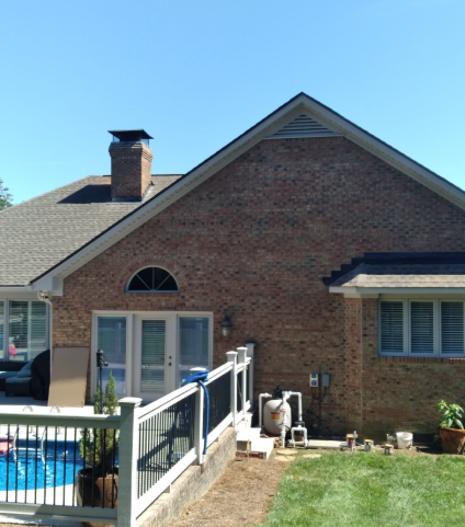 A brick house exterior with a white deck, pool, and swimming pool pump equipment in the backyard under a clear blue sky.
