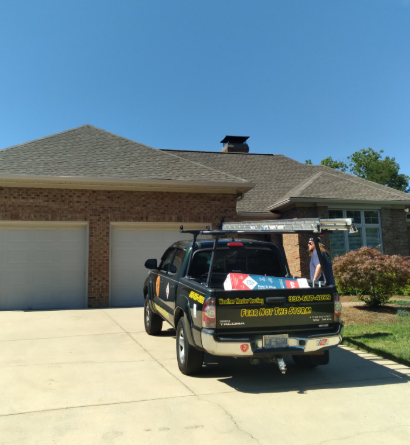 A black work truck parked in the driveway of a brick house with a gray shingled roof under a clear blue sky.