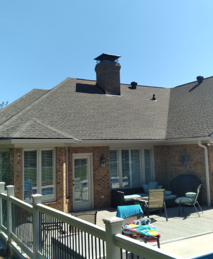 A brick house with a dark shingled roof, a chimney, and a patio set on a concrete pool deck.