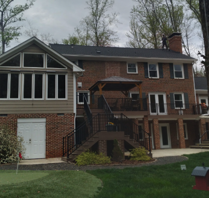 A two-story brick and siding house with a backyard deck, gazebo, and a person working on the roof.