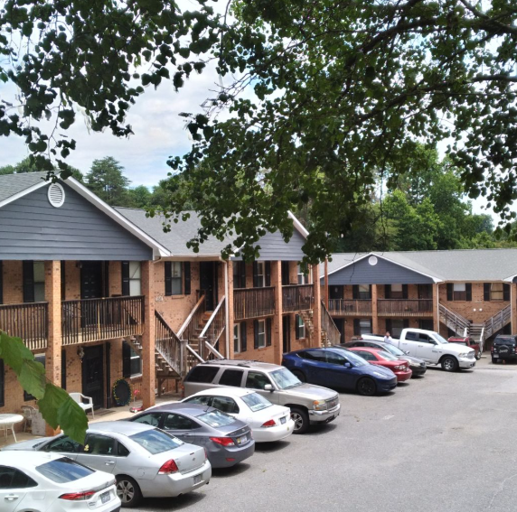 A multi-story brick apartment complex with wooden balconies and a parking lot filled with various cars.