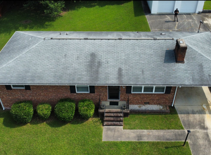 An aerial view of a single-story brick house with a gray shingled roof, front walkway, and green lawn.