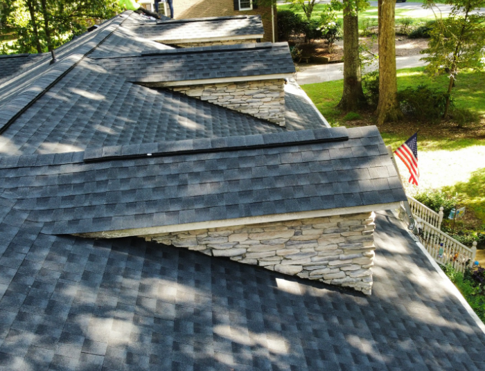 A view from above showing a dark shingled roof with two stone dormers and an American flag in the background.