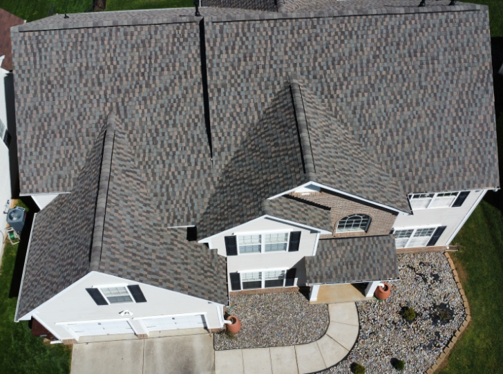 Aerial view of a two-story suburban house with a gray shingled roof, a front garage, and a landscaped front yard.
