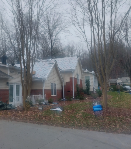A residential house with brick and beige siding under repair, with metal roofing panels visible on the roof.