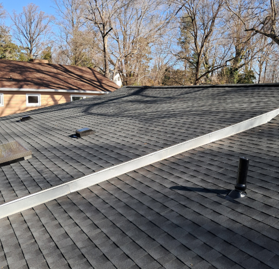 A high-angle view of a dark shingled roof with a long white flashing seam, a plumbing vent, and roof vents.