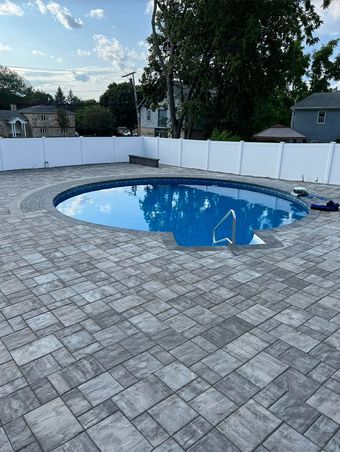 A swimming pool is surrounded by a brick patio and a white fence.