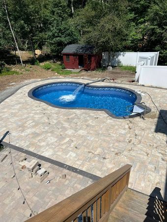 A large swimming pool is surrounded by a patio and a wooden deck.