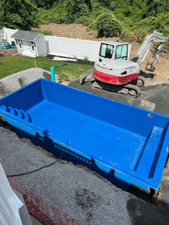 A blue swimming pool is being built in a backyard with a bulldozer in the background.