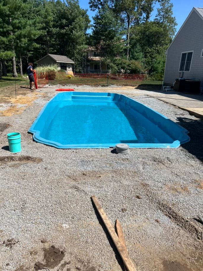 A blue swimming pool is being built in the backyard of a house.