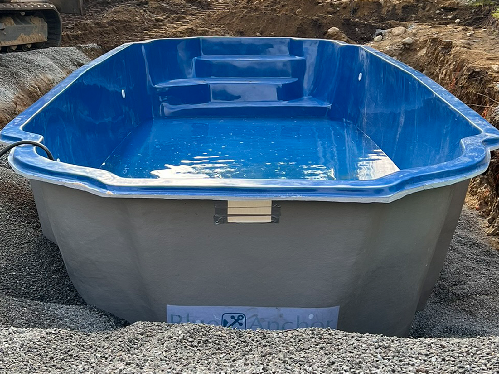 A large blue swimming pool is sitting on top of a pile of gravel.