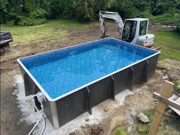A swimming pool is being built in a backyard with a bulldozer in the background.