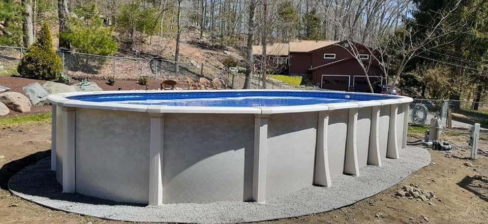 A large swimming pool is sitting in the dirt in front of a house.