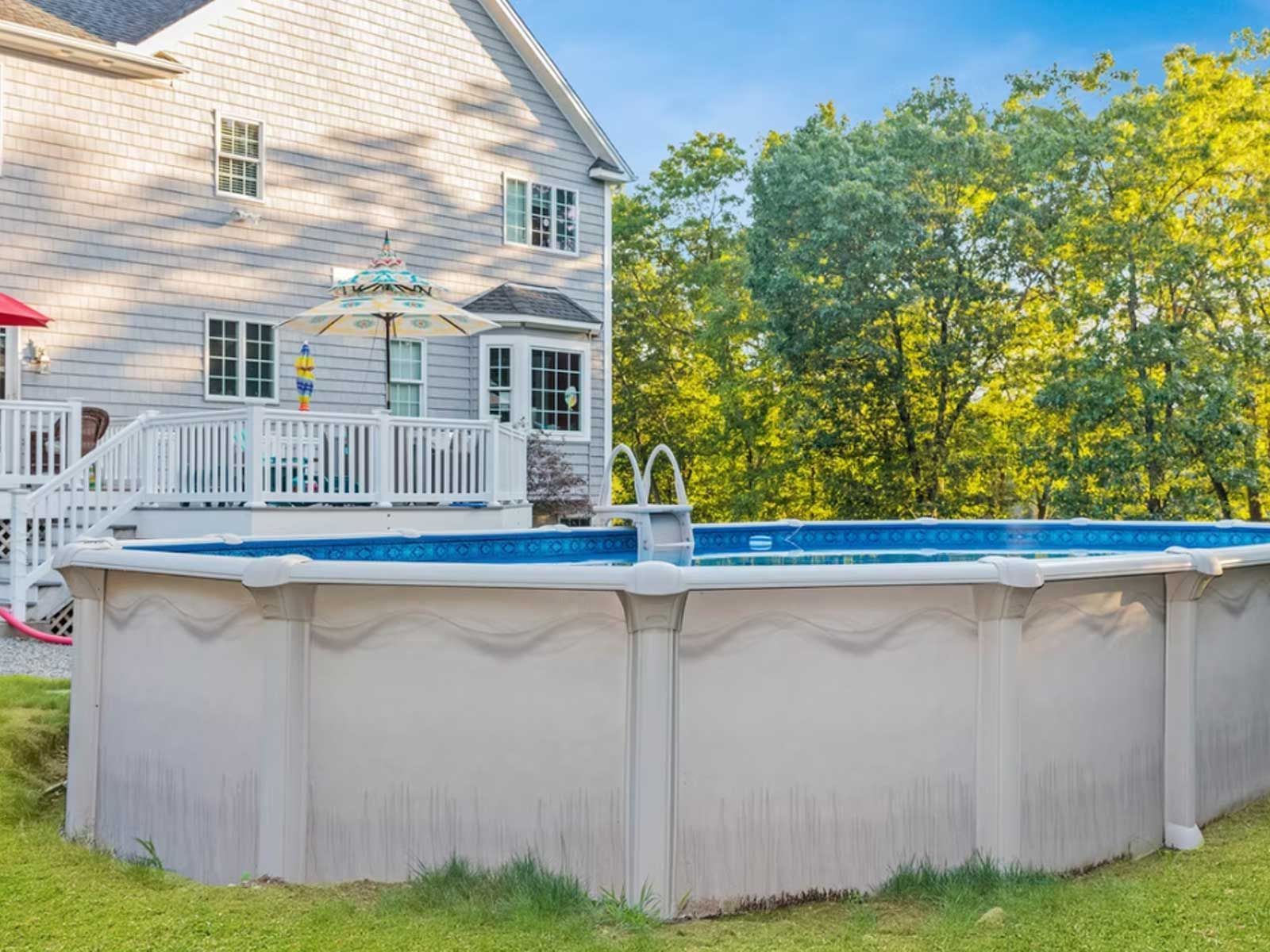 A large swimming pool is sitting in the grass in front of a house.