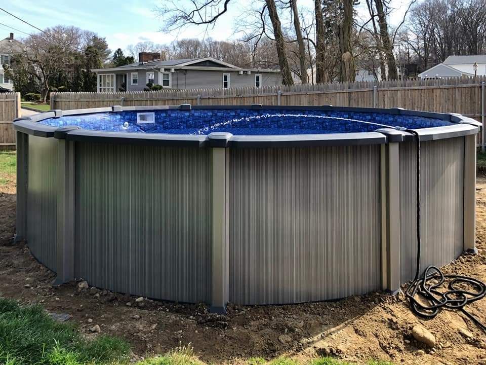 A large swimming pool is sitting in the dirt in a backyard.