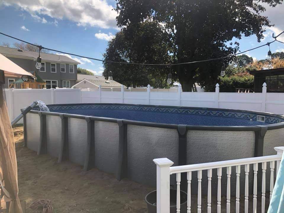 A large swimming pool is sitting in a backyard next to a white fence.