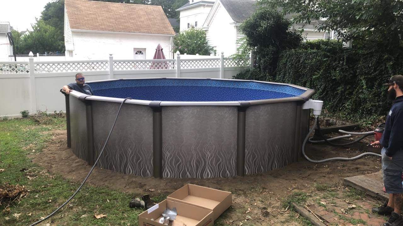 A man is standing next to a large swimming pool in a backyard.