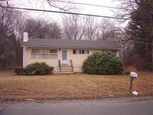 Yellow ranch-style house with bushes, bare trees, and a mailbox on a brown lawn.