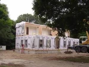 Modular home under construction; two-story structure, siding, windows, crane in the background.