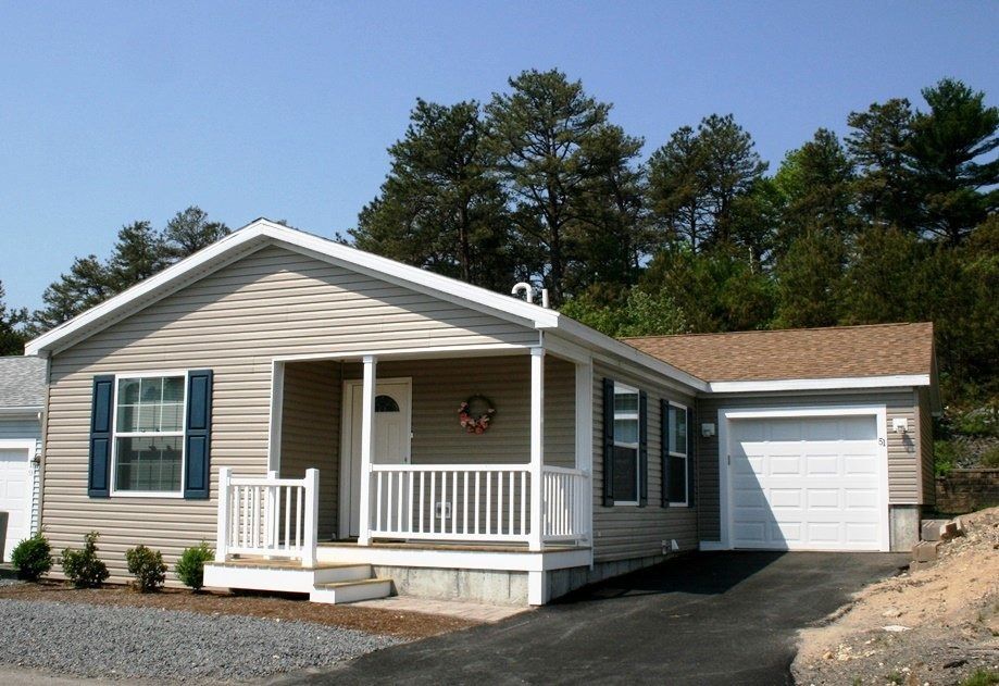 Tan one-story house with blue shutters, white porch, and attached garage; trees in the background.