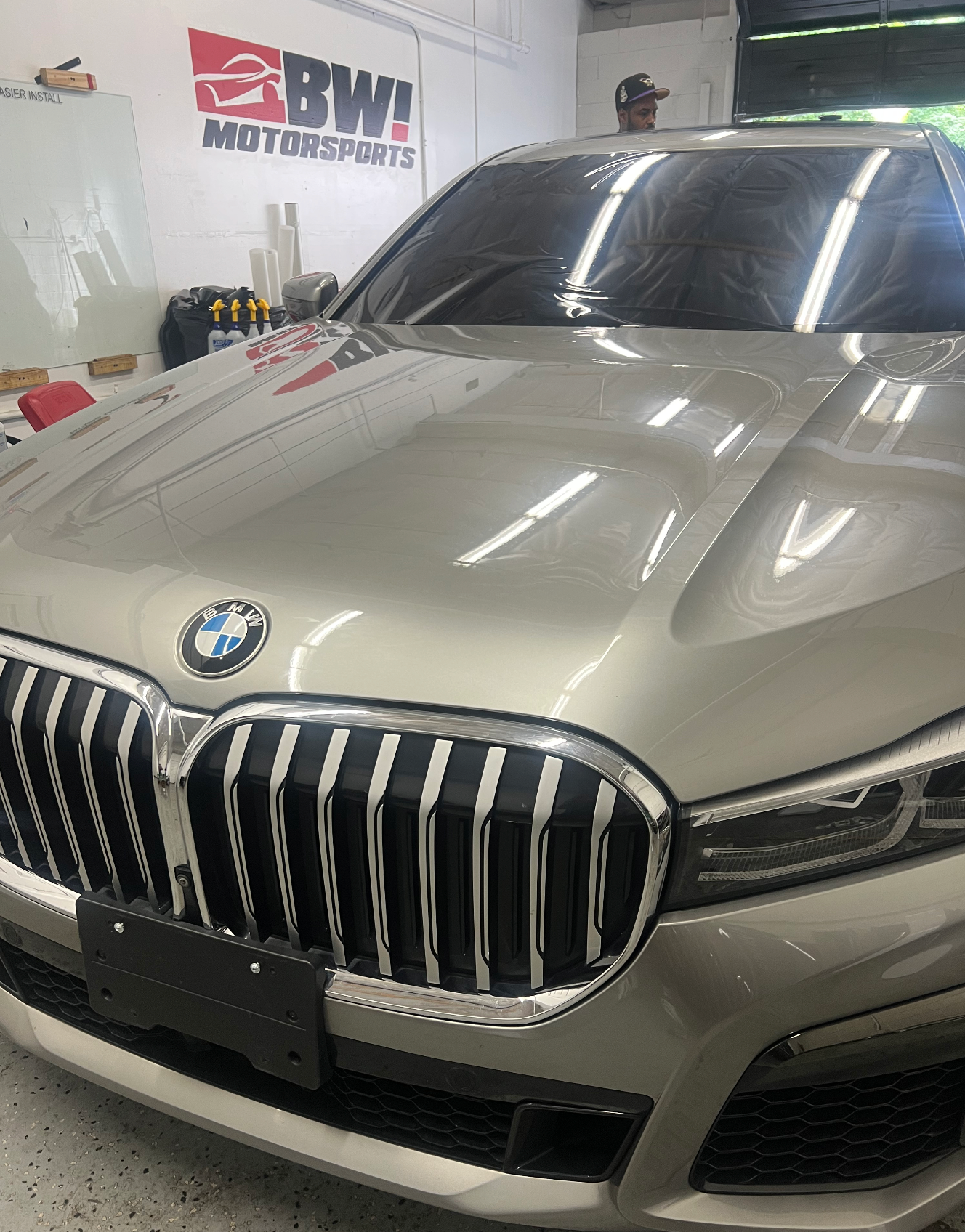 Silver BMW car in a garage with tinting film on the windows, a BW! Motorsports sign in the background.