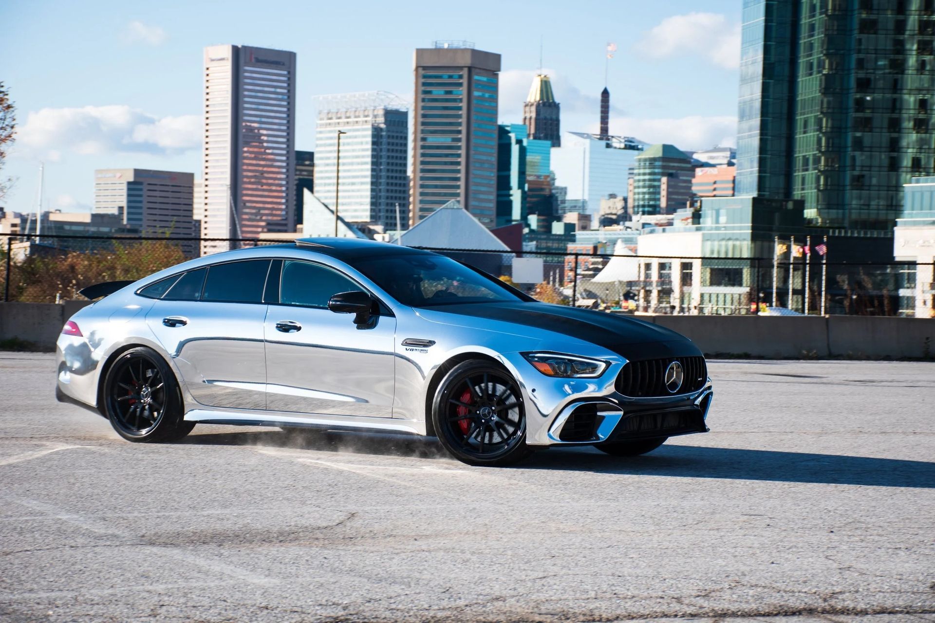 Silver car on a paved lot with city skyline in background.