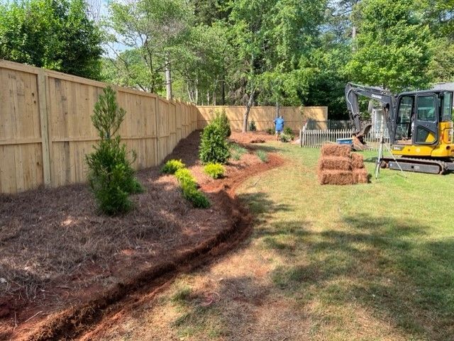 a yellow excavator is working in a backyard next to a wooden fence