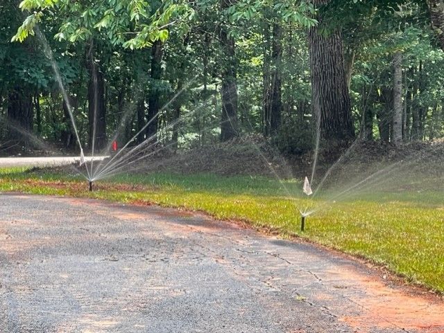 a row of sprinklers spraying water on a lush green lawn