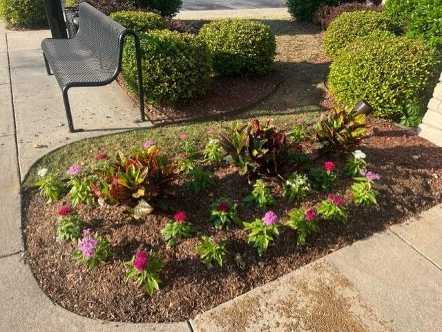a bench is sitting next to a garden with flowers and bushes